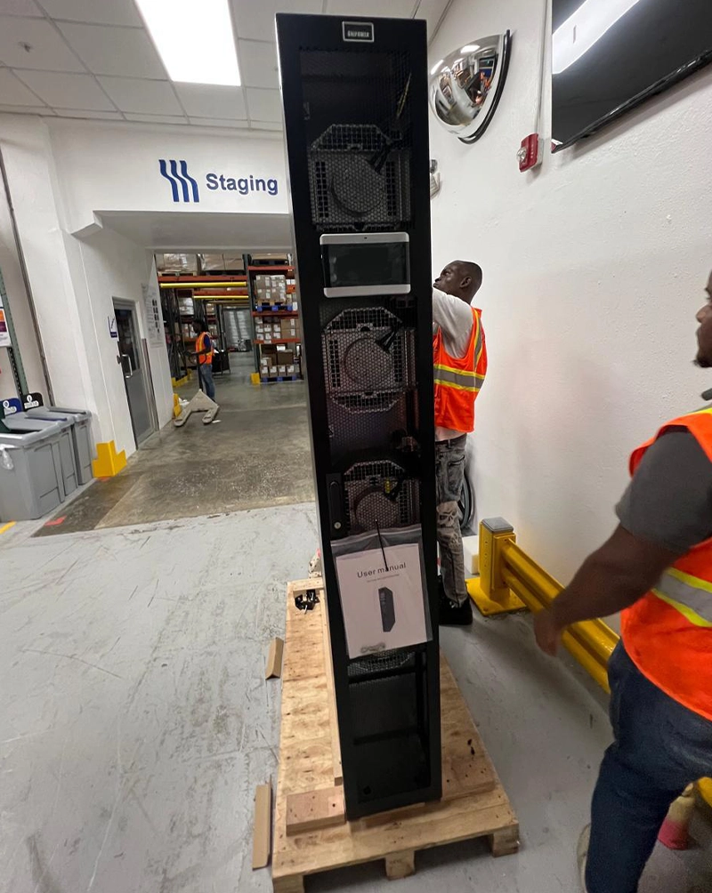 Dos operarios trasladan sobre un palé la unidad vertical recién recibida, con sus ventiladores a la vista y el manual todavía pegado